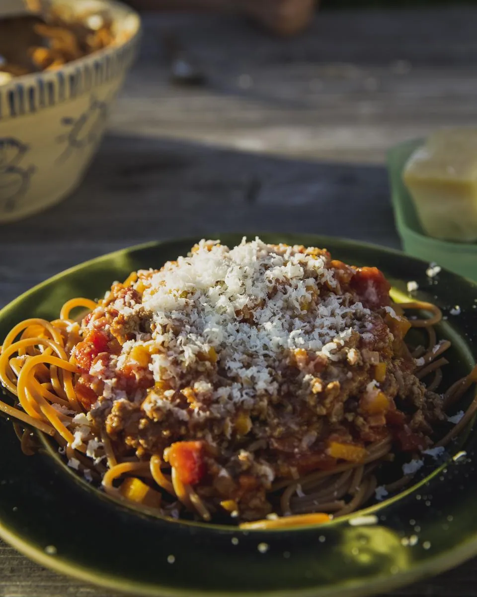 A bowl of spaghetti bolognese with grated cheese on a dark table